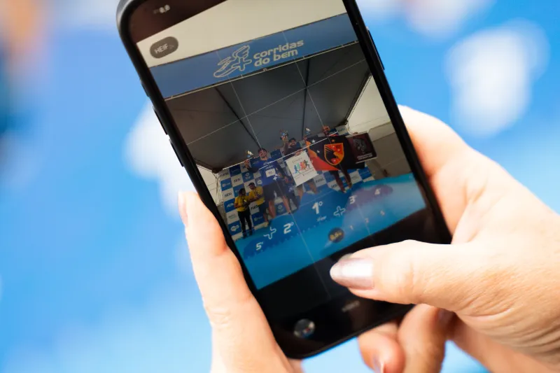 Detalhe: mulher fotografa, com celular, premiação no pódio